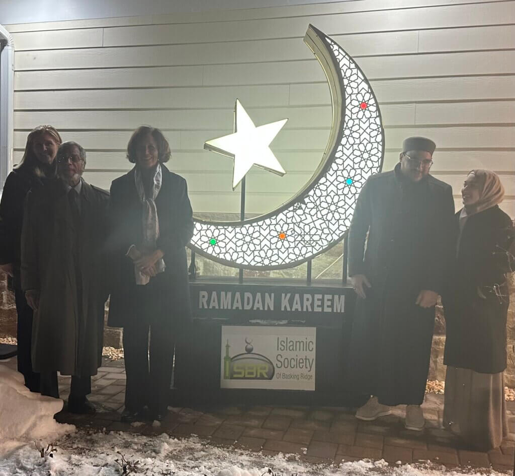 Mayor Ana Duarte McCarthy with 4 other people at the Islamic Society of Basking Ridge Crescent Lighting. There is a lit up crescent and star behind them.